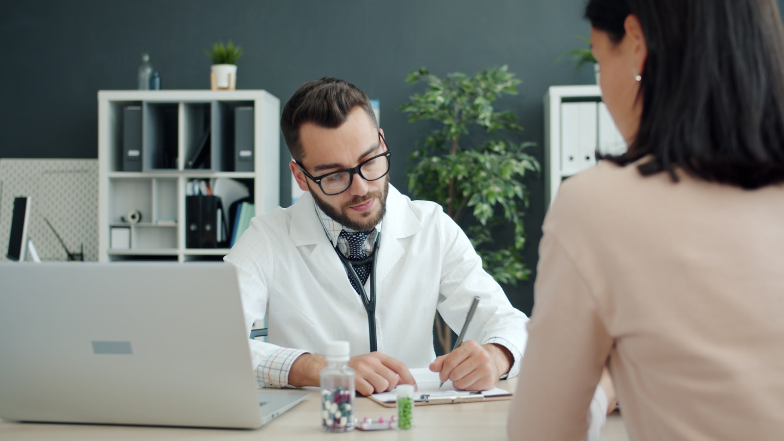 Doctor writing notes while patient sits opposite, life